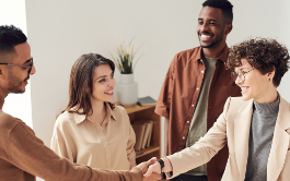 Four individuals shaking hands with one another while smiling.